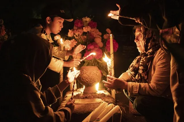 People hold candles over a tomb decorated with flowers at a cemetery in Atzompa, Mexico, late Tuesday, October 31, 2023. In a tradition that coincides with All Saints Day on Nov. 1 and All Souls Day on Nov. 2, families decorate graves with flowers and candles and spend the night in the cemetery, eating and drinking as they keep company with their dearly departed. (Photo by Maria Alferez/AP Photo)
