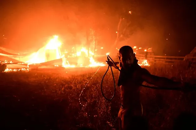 A man uses a water hose during a wildfire in Adames area, in northern Athens, Greece, Tuesday, August 3, 2021.Thousands of people fled their homes north of Athens on Tuesday as a wildfire broke out of the forest and reached residential areas. The hurried evacuations took place just as Greece grappled with its worst heat wave in decades. (Photo by Michael Varaklas/AP Photo)