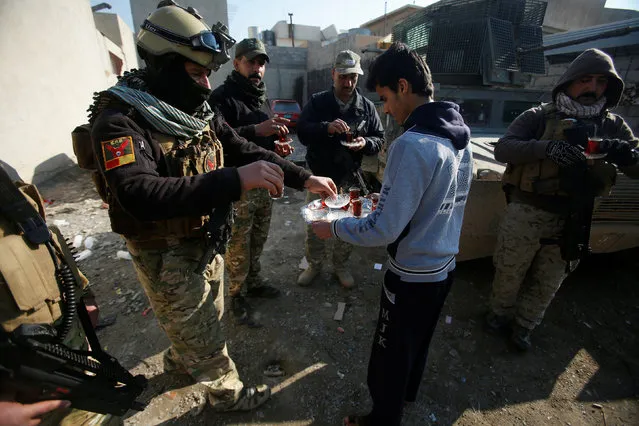 A civilian hands out tea to members of the Iraqi rapid response forces during a battle with the Islamic State militants in the Mithaq district of eastern Mosul, Iraq, January 5, 2017. (Photo by Khalid al Mousily/Reuters)