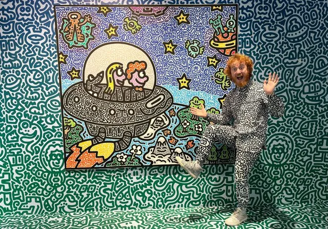 This photo taken on November 16, 2023 shows British artist Sam Cox, better known as Mr. Doodle, posing for a picture with his piece “The Doodles Leave Earth” at Pearl Lam Galleries in Hong Kong. A major Hong Kong transport hub was taken over on November 19, 2023 by googly-eyed aliens, extraterrestrial jellyfish and an organised chaos of eccentric characters – all part of a live doodling performance by British artist Sam Cox, better known as Mr. Doodle. (Photo by Dene Chen/AFP Photo)