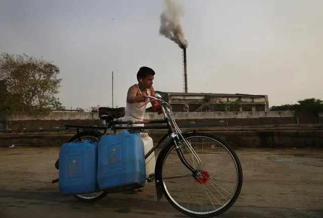 An Indian man pushes a cycle carrying water cans as smokes rises from a biomedical waste plant in Mumbai, India, Thursday, April 9, 2015. (Photo by Rafiq Maqbool/AP Photo)