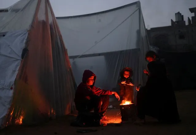 Displaced Palestinians, who fled their houses due to Israeli strikes, warm themselves by a fire on a rainy cold day at a tent camp, amid the ongoing conflict between Israel and Hamas, in Rafah in the southern Gaza Strip on January 26, 2024. (Photo by Saleh Salem/Reuters)