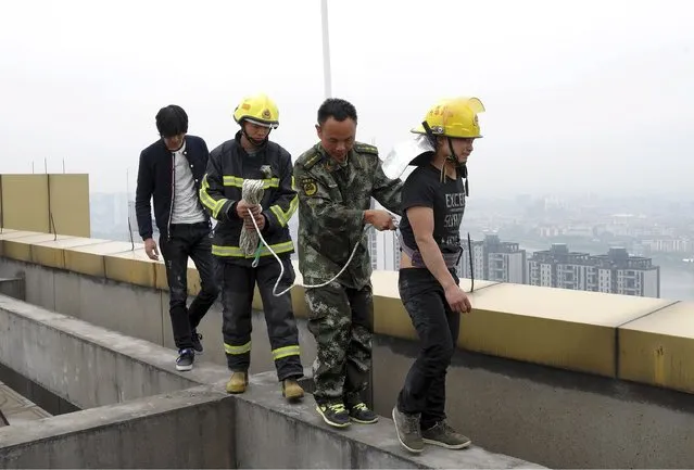 A man (R), who attempted to commit suicide, cries as he is taken to safety by rescuers on the roof of a 35-storey building, in Jinhua, Zhejiang province, China, April 24, 2015. (Photo by Reuters/Stringer)