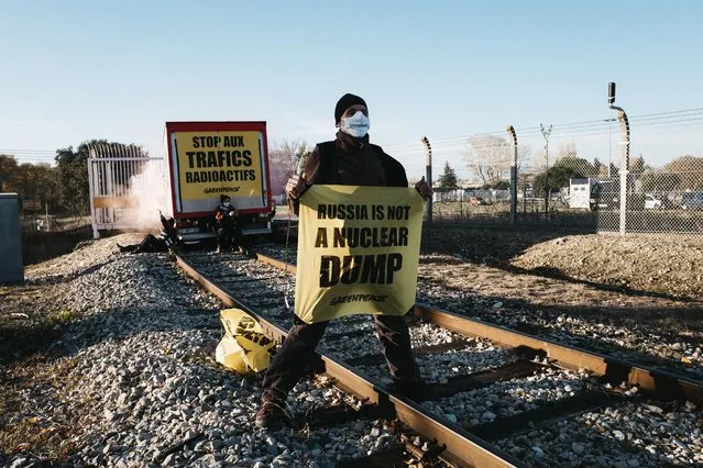 A Greenpeace activist holds a banner during an attempt to block a railway access in southern France where Greenpeace say a convoy of reprocessed uranium is due to leave to be exported to Russia, in Pierrelate, southern France, Tuesday, November 16, 2021. The railway access is located in Pierrelatte, just outside the Orano plant where radioactive material is processed and stored. (Photo by Mait Baldi/Greenpeace via AP Photo)