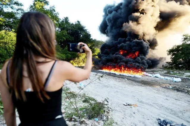A woman films with her phone the incineration of packages of cocaine, part of a high seas drug seizure of 135 bundles by Salvadoran Naval Force, at a police base in Ilopango, El Salvador, November 29, 2021. (Photo by Jessica Orellana/Reuters)