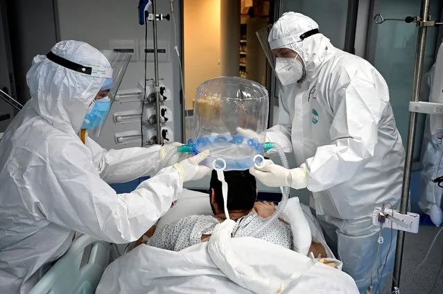 Medical staff members help a patient to wear a new non-invasive technology that can reduce the need of intubation at Covid-19 intensive care unit (ICU) at The Institute of Clinical Cardiology (ICC) in Rome, on December 30, 2021. (Photo by Alberto Pizzoli/AFP Photo)