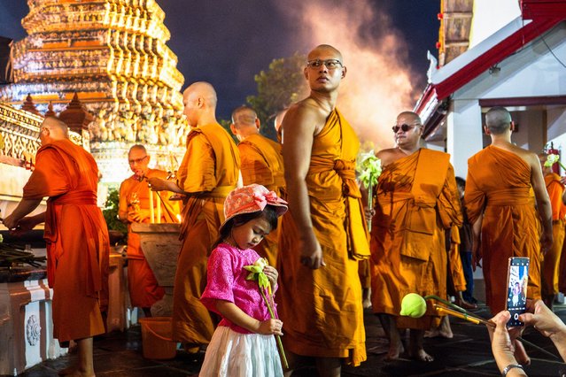 A young worshipper holds a lotus flower as Buddhist monks gather at Wat Arun Buddhist temple during Asaha Bucha day in Bangkok on July 20, 2024. (Photo by Chanakarn Laosarakham/AFP Photo)