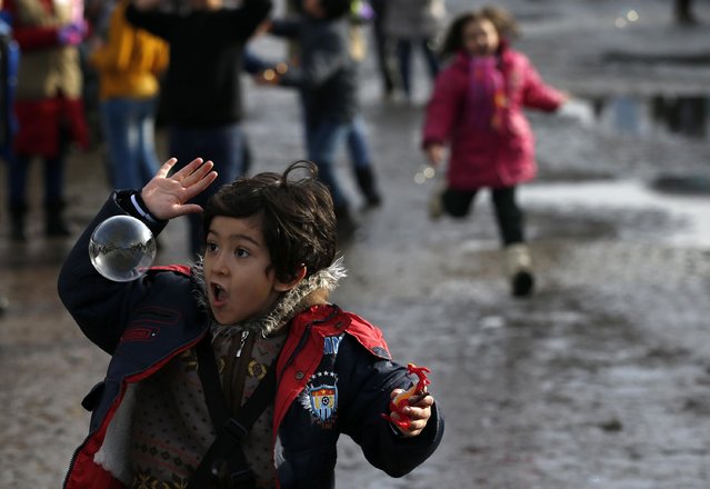 Migrant children play with soap bubbles as they wait to be taken to the train station in Sid, in Adasevci, about 100 km west from Belgrade, Serbia, Monday, January 11, 2016. (Photo by Darko Vojinovic/AP Photo)