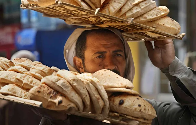 A bread vendor carries a tray of Egyptian traditional “Baladi” flatbread, outside a bakery, in the Old Cairo district of Cairo, Egypt, Tuesday, March 22, 2022. Egypt's Central Bank raised its key interest rate Monday for the first time since 2017, citing inflationary pressures triggered by the coronavirus pandemic and Russia's war in Ukraine, which hiked oil prices to new records. (Photo by Amr Nabil/AP Photo)