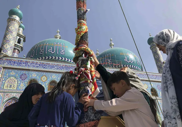 Afghan Shiite children and women kiss the holy mace for blessings during celebrations of Nowruz, the Persian new year, as Taliban soldiers  stand guard at the Kart-e-Sakhi shrine in Kabul, Afghanistan, Monday, March 21, 2022. Nowruz is an ancient Persian festival, celebrated on the first day of spring in many countries including Afghanistan, Tajikistan, and Iran. (Photo by Mohammed Shoaib Amin/AP Photos)