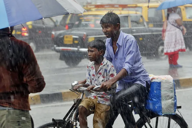 An Indian cyclist pedals with a child during heavy rain in Mumbai, Maharashtra state, India, Friday, July 24, 2015. Several parts of the city witnessed heavy rain Friday. The monsoon rains which usually hit India from June to September are crucial for farmers whose crops feed hundreds of millions of people. (Photo by Rajanish Kakade/AP Photo)