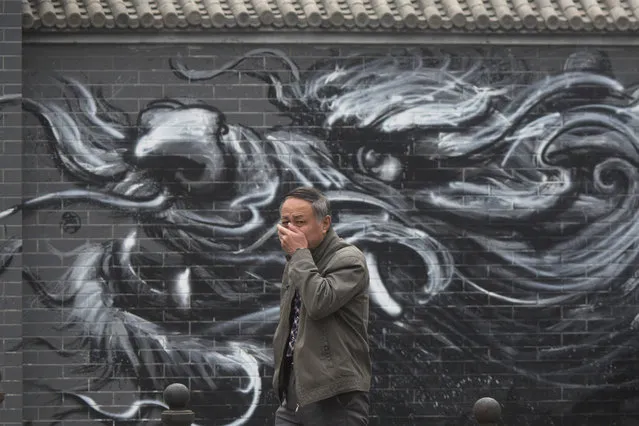 In this file photo taken Tuesday, December 20, 2016, a Chinese man places his hand over his mouth as he walks past graffiti of a dragon during a day of heavy pollution in Beijing, China. (Photo by Ng Han Guan/AP Photo)