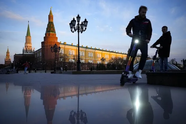 Youth ride scooters in Manezhnaya Square near Red Square and the Kremlin after sunset in Moscow, Russia, Wednesday, April 20, 2022. (Photo by Alexander Zemlianichenko/AP Photo)