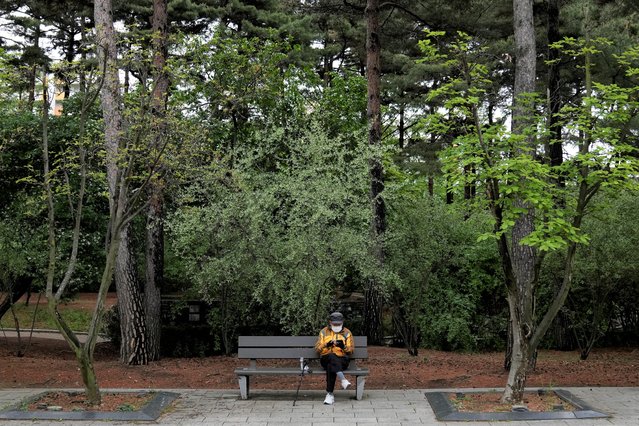 A man wearing a face mask to help curb the spread of the coronavirus sits on a bench while maintaining social distancing at a park in Seoul, South Korea, Friday, April 29, 2022. (Photo by Lee Jin-man/AP Photo)