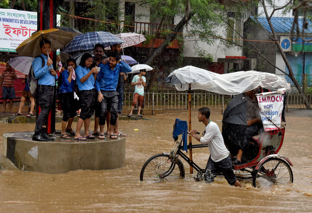 College students take shelter at a traffic point as a man paddles his rickshaw through a flooded road during heavy rain in Guwahati, India, June 13, 2017. (Photo by Anuwar Hazarika/Reuters)