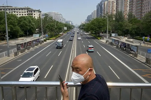 A man wearing a face mask stands on a bridge over an expressway in Beijing, Thursday, May 19, 2022. Parts of Beijing on Thursday halted daily mass testing that had been conducted over the past several weeks, but many testing sites remained busy due to requirements for a negative COVID test in the last 48 hours to enter some buildings in China's capital. (Photo by Mark Schiefelbein/AP Photo)
