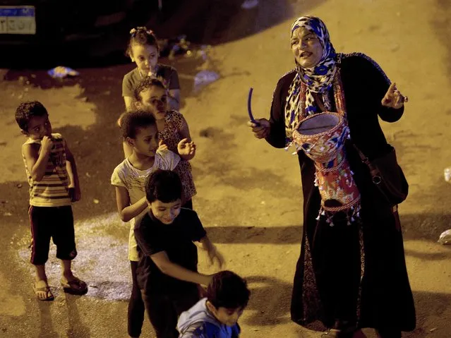 In this Monday, June 12, 2017 photo, Hajja Dalal, a 43-year-old “mesaharati”, or dawn caller, is surrounded by children as she wakes people up for a meal before sunrise, during the Islamic holy month of Ramadan, in Ard Besary district in Cairo, Egypt. (Photo by Amr Nabil/AP Photo)
