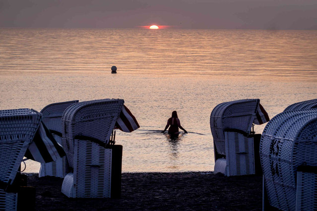 A woman goes for a swim in the Baltic Sea in Timmendorfer Strand, Germany, as the sun rises on Friday, July 19, 2024. (Photo by Michael Probst/AP Photo)