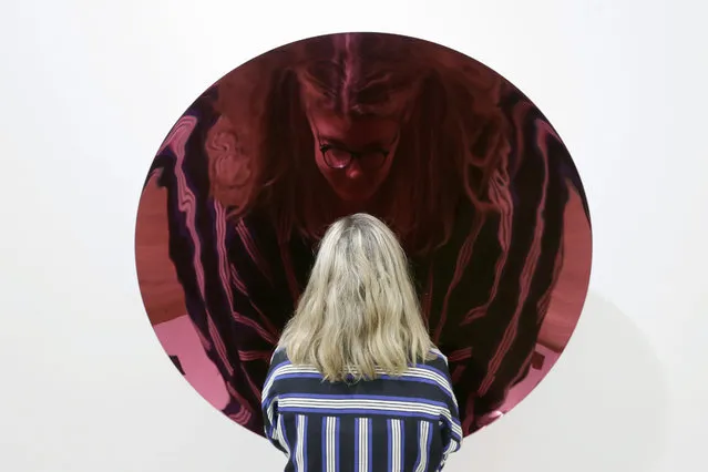 A Bonhams employee poses for a picture with Anish Karpoor's 2012 “Untitled”, a concave metal disk coated in enamel, in London, Friday, June 26, 2015. (Photo by Tim Ireland/AP Photo)