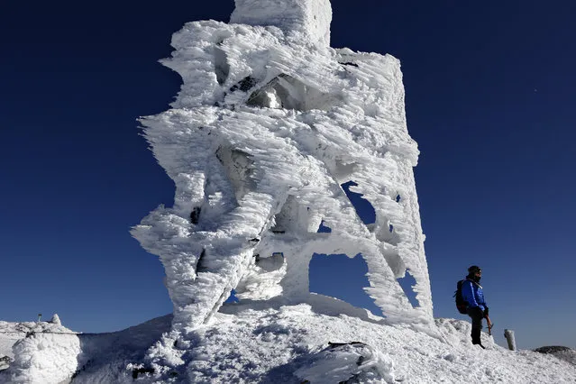 Douglas Ciampi of Westminster, Mass., stands next to a rime ice-covered antenna while taking in the view from the summit of Mount Washington, N.H., Sunday, February 23, 2020. Rime ice forms when supercooled moisture hits a solid surface. Ciampi's 5-hour hike was rewarded by exceptionally clear conditions allowing for a visibility of 100 miles from the northeast's highest peak. (Photo by Robert F. Bukaty/AP Photo)