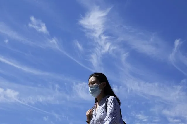 A woman wearing a mask passes by a blue sky with wispy clouds during a hot day, Thursday, July 14, 2022, in Beijing. (Photo by Ng Han Guan/AP Photo)