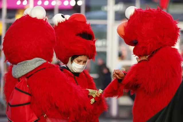 A mask-wearing costumed character in Times Square looks through bills during a lull in activity Thursday, March 12, 2020, in New York. Earlier Thursday, Gov. Andrew Cuomo banned gatherings of 500 or more people. (Photo by Kathy Willens/AP Photo)