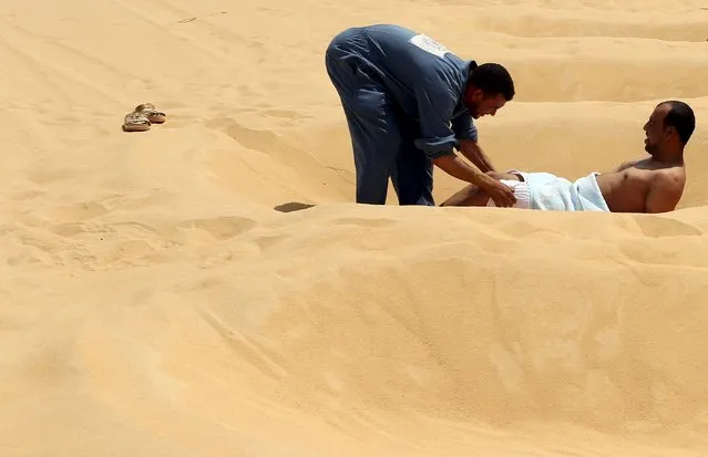 A worker helps a patient take off his clothes before he's buried in the sand in Siwa, Egypt, August 11, 2015. (Photo by Asmaa Waguih/Reuters)