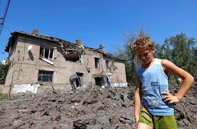 A boy stands in front of a residential building damaged by recent shelling in the course of the Ukraine-Russia conflict in the Russian-controlled settlement of Panteleymonivka in the Donetsk region, Ukraine on August 17, 2022. (Photo by Alexander Ermochenko/Reuters)