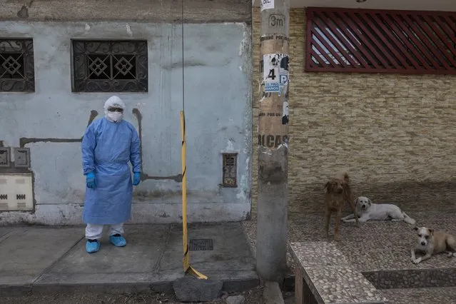 A doctor waits at the front door of a person's home before doing a new coronavirus fast test in Lima, Peru, Monday, April 13, 2020. Peruvians can call a telephone number to report that they have symptoms of COVID-19, and the state organized medical brigades will visit and do rapid tests to confirm or rule out new COVID-19 infections. (Photo by Rodrigo Abd/AP Photo)