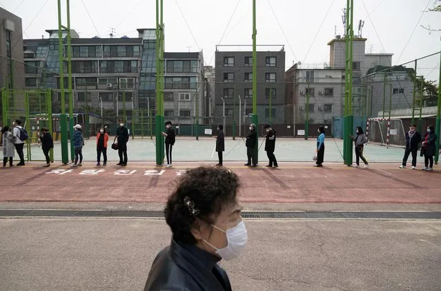 A woman walks past a queue of voters wearing masks, in an effort to prevent the spread of the coronavirus disease (COVID19), while waiting to cast their ballots at a polling station in Seoul, South Korea, April 15, 2020. (Photo by Kim Hong-Ji/Reuters)