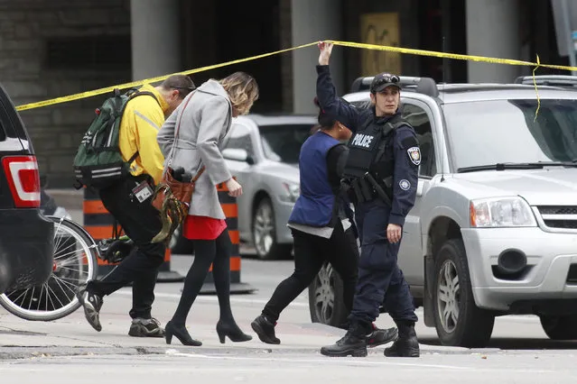 A Ottawa police officer holds up a length of police tape for pedestrians leaving the downtown area following shooting incidents in Ottawa October 22, 2014. (Photo by Blair Gable/Reuters)