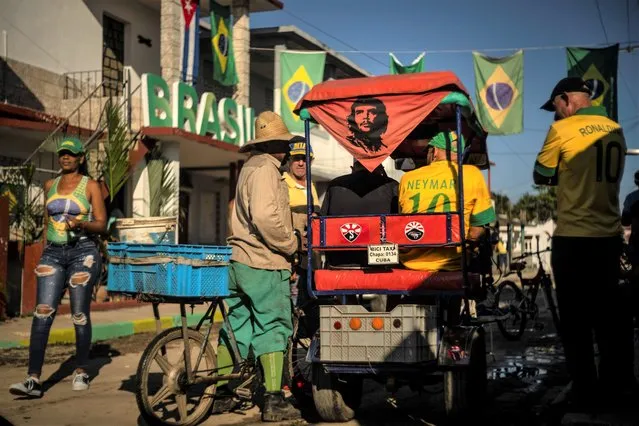 Cuban fans of the Brazilian soccer team talk before the match between Brazil and Switzerland, next to a rickshaw decorated with an image of Ernesto “Che” Guevara in Bauta, Cuba, Monday, November 28, 2022. People in the municipality of Bauta have been getting together for every World Cup over the last 20 years to support Brazil, who won 1-0. (Photo by Ramon Espinosa/AP Photo)