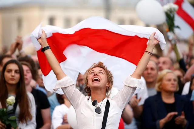 A demonstrator reacts while holding the historical white-red-white flag of Belarus during an opposition demonstration to protest against police violence and to reject the presidential election results near the Government House in Independence Square in Minsk, Belarus on August 14, 2020. (Photo by Vasily Fedosenko/Reuters)