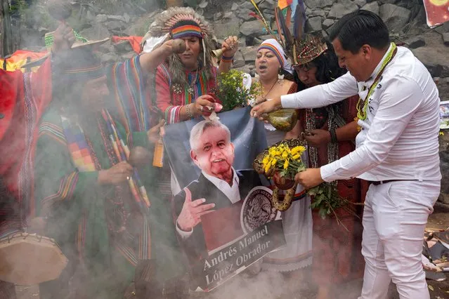 Peruvian shamans equipped with coca leaves, swords, smoking ceramic pots, incense, and a live snake hold a poster of Mexico's President Andres Manuel Lopez Obrador while executing a ritual at the top of a hill over Lima to deliver their predictions for the coming year on December 28, 2022. (Photo by Cris Bouroncle/AFP Photo)