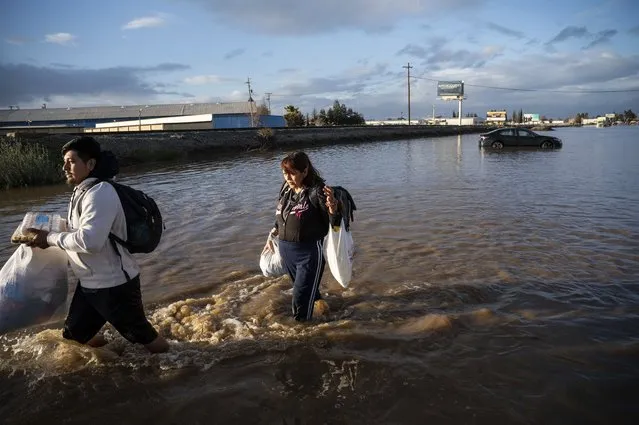 Angeles Molina carries belongings from her flooded Merced, Calif., home on Tuesday, January 10, 2023. Following days of rain, Bear Creek overflowed its banks leaving dozens of homes and vehicles in the neighborhood surrounded by floodwaters. (Photo by Noah Berger/AP Photo)