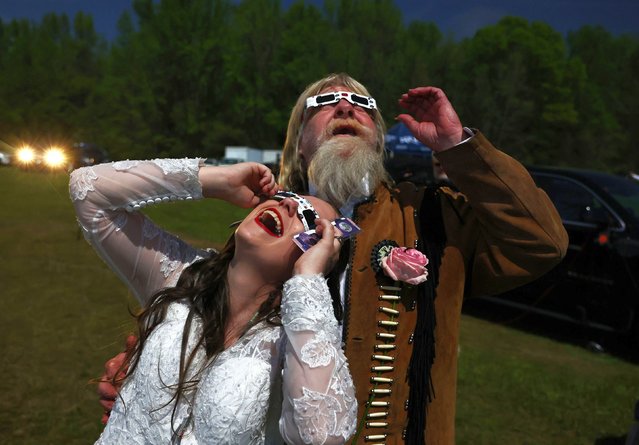 A bride and groom view the solar eclipse amid a darkened sky after marrying at a mass wedding at the Total Eclipse of the Heart festival on April 8, 2024 in Russellville, Arkansas. Millions of people have flocked to areas across North America that are in the “path of totality” in order to experience a total solar eclipse. During the event, the moon will pass in between the sun and the Earth, appearing to block the sun. (Photo by Mario Tama/Getty Images)