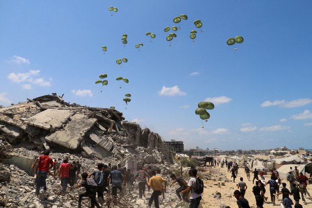 Palestinians run towards parachutes carrying aid packages airdropped over northern Gaza Strip on August 7, 2025. (Photo by Ebrahim Hajjaj/Reuters)