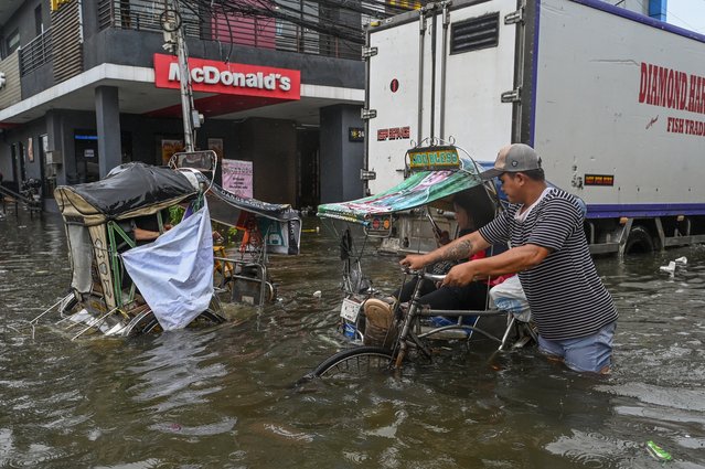 People wade through a flooded area in Malabon, metro Manila on July 24, 2025. The Philippines shut down schools and cancelled flights on July 24 as torrential rains driven by a typhoon and a separate tropical storm pounded the country's northern island of Luzon. (Photo by Jam Sta Rosa/AFP Photo)