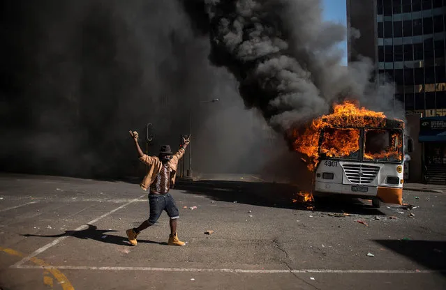A student gestures near a burning bus during clashes with riot police following a protest over University tuition fees on October 10, 2016 in Johannesburg. South African student protesters and police clashed in renewed violence in Johannesburg as attempts to re-open Wits University descended into running battles on campus. Protesters throwing rocks were dispersed by riot police using tear gas, rubber bullets and stun grenades as pressure ratchets up on campuses across the country over tuition fees. (Photo by Mujahid Safodien/AFP Photo)