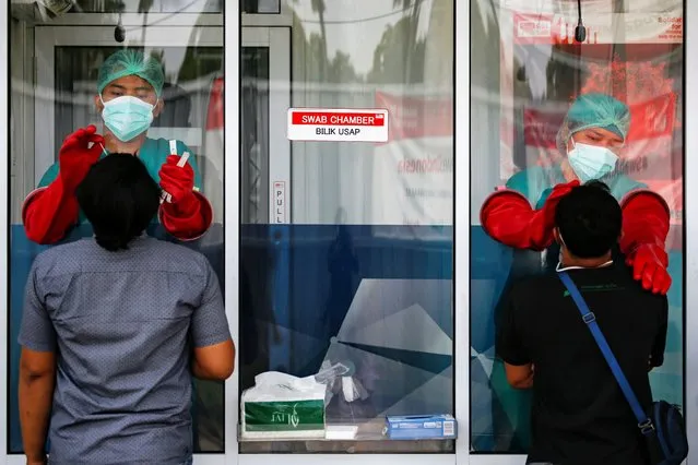 Medical workers wearing personal protective equipments (PPE) utilize a swab chamber as they collect swab samples from men to be tested for the coronavirus disease (COVID-19), as the outbreak continues in Jakarta, Indonesia, Indonesia, November 24, 2020. (Photo by Willy Kurniawan/Reuters)