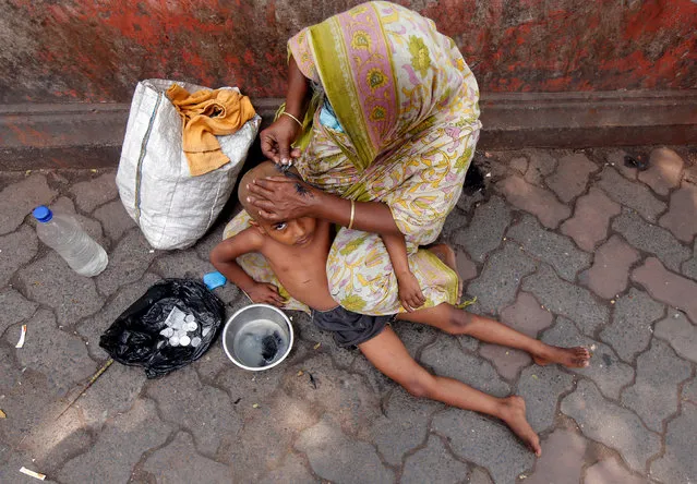A woman uses a razor blade to shave her son's head on a pavement along a market area in Kolkata, India, April 10, 2018. (Photo by Rupak De Chowdhuri/Reuters)