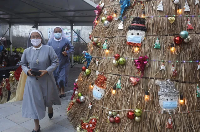 Nuns wearing face masks to protect against coronavirus walk pass a Christmas tree with a coronavirus-themed decoration before Christmas mass service at a church in Bali, Indonesia on Thursday, December 24, 2020. (Photo by Firdia Lisnawati/AP Photo)