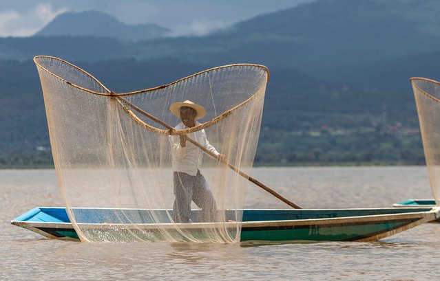 A fisherman uses the butterfly net technique to fish near the island of Janitzio in Patzcuaro lake, Michoacan state, Mexico on July 16, 2024. The Patzcuaro municipality works with residents on a program to recover the water level of lake Patzcuaro, seriously affected by drought. (Photo by Enrique Castro/AFP Photo)