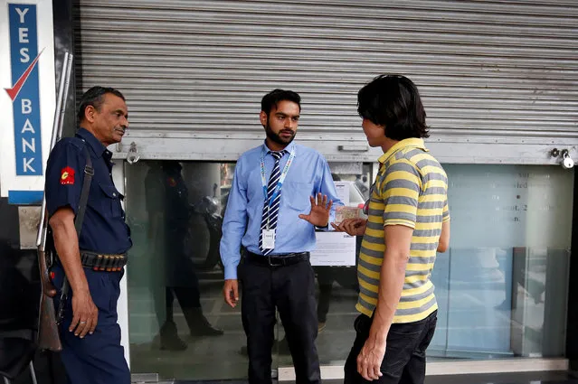 An employee speaks with a man holding 1000 rupee notes outside a Yes Bank branch in New Delhi, India, November 9, 2016. (Photo by Cathal McNaughton/Reuters)