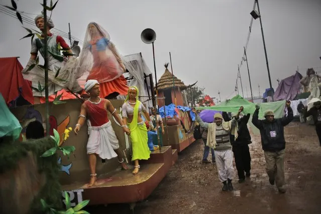 Workers cover themselves from rain as they walk past tableaux during a media preview displaying a glimpse of culture of different parts of India, in New Delhi, India, Thursday, January 22, 2015. (Photo by Altaf Qadri/AP Photo)