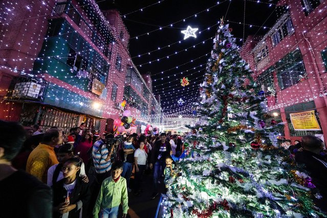 People throng around a Christmas tree on a decorated street in Bow Barrack, a colonial settlement during WWII, on the eve of Christmas in Kolkata, India, Tuesday, December 24, 2024. (Photo by Bikas Das/AP Photo)