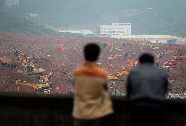 People watch rescuers using machinery to search for potential survivors following a landslide in Shenzhen, in south China's Guangdong province, Monday, December 21, 2015. A mountain of excavated soil and construction waste buried dozens of buildings when it swept through an industrial park Sunday. (Photo by Andy Wong/AP Photo)