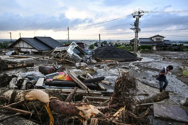 A man walks past debris from flooding in the road in the city of Kurume, Fukuoka prefecture, on July 10, 2023, after heavy rains hit wide areas of Kyushu island. (Photo by Kazuhiro Nogi/AFP Photo)