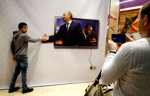 A boy poses for a photo with a poster depicting Russian President Vladimir Putin, left in photo, and U.S. President Barack Obama in a shopping mall in St.Petersburg, Russia, Sunday, January 3, 2016. (Photo by Dmitry Lovetsky/AP Photo)
