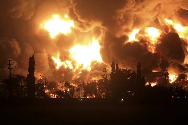 Cars pass by as fire razes through Pertamina Balongan Refinery in Indramayu, West Java, Indonesia, early Monday, March 29, 2021. Hundreds of people were evacuated from a nearby village after the massive fire broke out at the refinery. (Photo by AP Photo/Stringer)